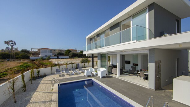 Ein modernes, zweistöckiges Haus mit Pool, Außenbereich und einem Windrad im Hintergrund.