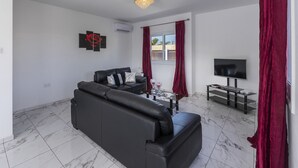 A modern living room with a black leather sofa, a flat-screen TV, and a marble-tiled floor. - Your Dream 5-star Escape: Protaras Villa 1483 (Paralimni)