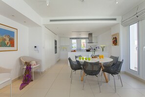 A modern kitchen with white cabinets, a central island, and a dining area with black wire chairs. - Imagine Your Family Renting This Luxury Beachfront Villa, Protaras Villa 1541 (Paralimni)