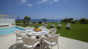 Ein Essbereich am Pool mit einem Tisch für vier Personen, mit Blick auf einen klaren, blauen Himmel und das Meer.