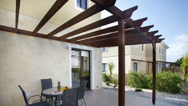 Eine Terrasse im Freien mit einer Pergola, einem Tisch mit Stühlen und einem kleinen Gartenbereich.