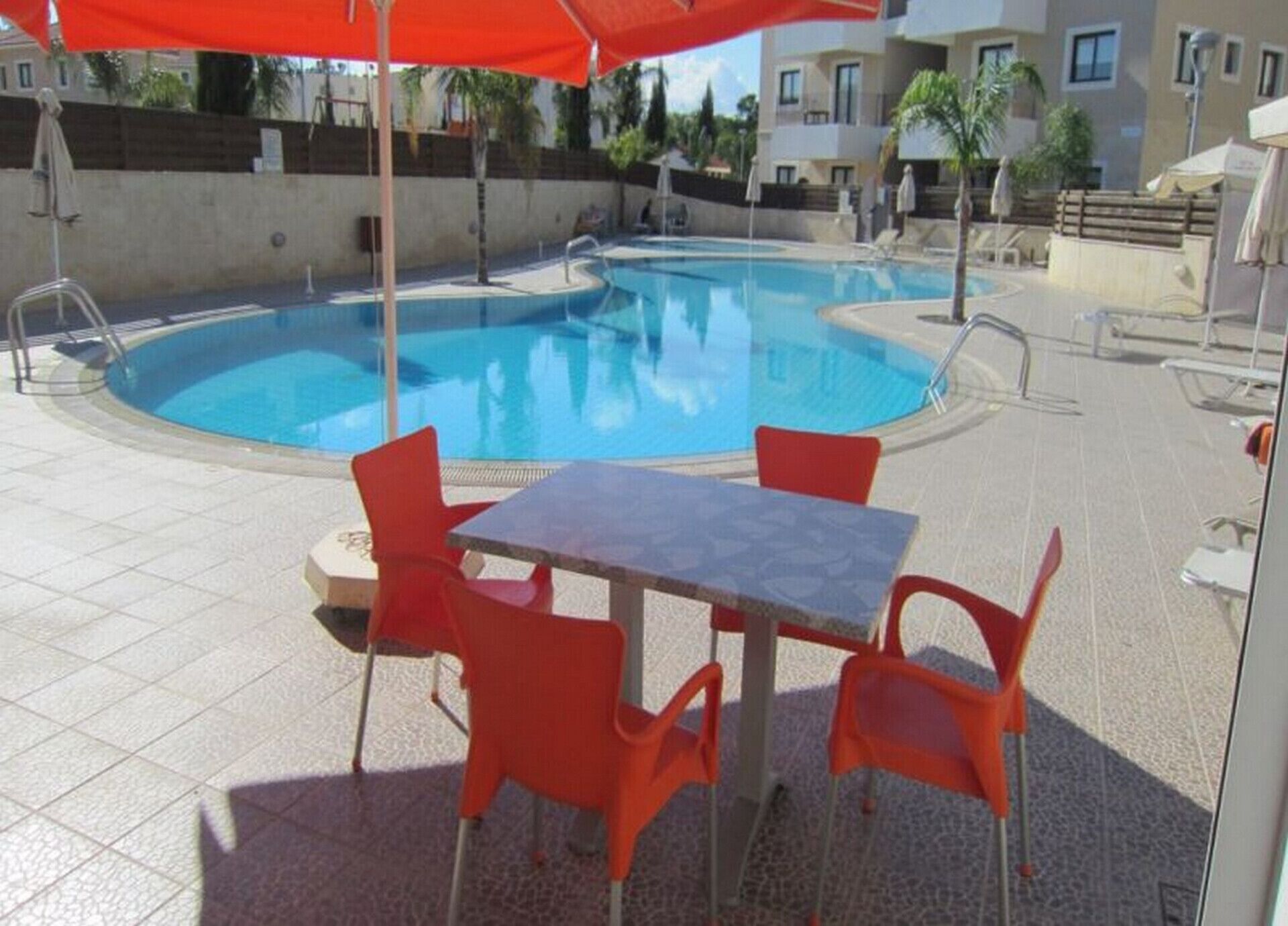 A swimming pool with red chairs and a table, surrounded by buildings.