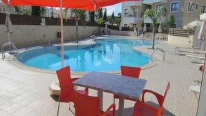 Ein Pool mit roten Stühlen und einem Tisch, umgeben von Gebäuden.