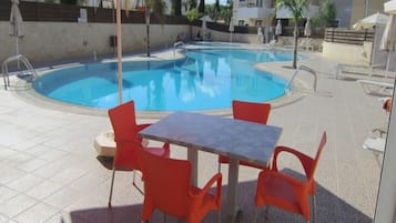 A swimming pool with red chairs and a table, surrounded by buildings.