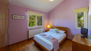 A bedroom with a bed, bedside lamp, window, radiator, and a TV on a wooden desk. - At Last You can Rent the Perfect Luxury Villa in Larnaca, Larnaca Villa 1392 (Pervolia)