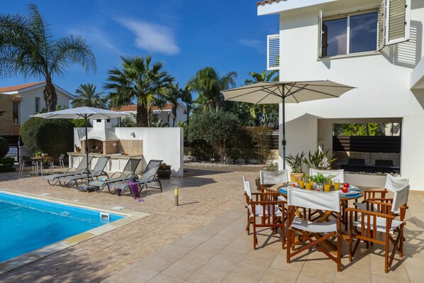 A poolside area with lounge chairs, a table with chairs, and a barbecue grill.