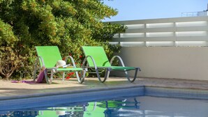 Ein Swimmingpool mit zwei grünen Liegestühlen und einer weißen Wand im Hintergrund.