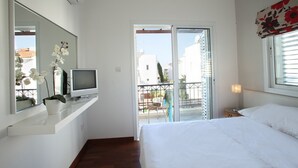 Ein Schlafzimmer mit Bett, Fernseher auf einem Regal, einem Balkon mit Geländer und einem Fenster mit Jalousien.