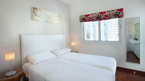 Ein Schlafzimmer mit einem Doppelbett, einem Nachttisch mit Lampe, einem Fenster mit Fensterläden und einem Spiegel an der Wand.