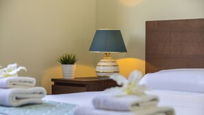A neatly made bed with white linens and a blue pillow, a bedside table with a lamp, a small potted plant, and folded towels. - The Secret to Enjoying Your 5 Star Villa Close to the Beach, Protaras Villa 1484 (Paralimni)