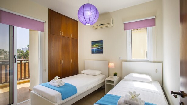 A hotel room with two single beds, a wooden wardrobe, a ceiling fan, a nightlight, and a window with a view of palm trees. - The Secret to Enjoying Your 5 Star Villa Close to the Beach, Protaras Villa 1484 (Paralimni)