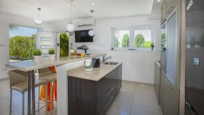 Een moderne keuken met een centraal eiland, een inbouwoven en een groot raam met uitzicht op groen.