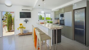 Een moderne keuken met een centraal eiland, roestvrijstalen apparatuur en een flatscreen televisie aan de wand.