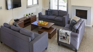 A living room with grey sofas, a coffee table, a flat-screen TV, and a fireplace. - Rent Your 5-star Villa With Private Pool Protaras Villa 1525 (Paralimni)