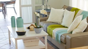 Ett vardagsrum med en soffa, ett soffbord, en krukväxt och en matplats med stolar och ett bord.