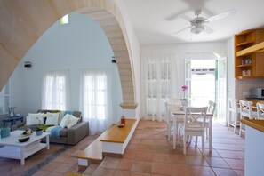 A spacious living area with a high arched ceiling, a dining area with white chairs, and a kitchen with wooden shelves. - Dream Family Escape: Protaras Villa 1542 (Paralimni)