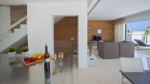 Un soggiorno moderno con un divano, una TV e un'area pranzo con tavolo, sedie e una bottiglia di vino.