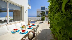 Area pranzo all'aperto con piscina, pareti bianche e vista sul mare.
