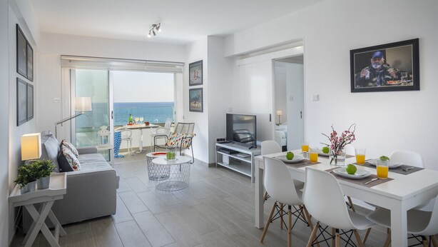 A modern living room with a balcony, a dining area, and a TV. - Fall in Love With This Luxury Beachfront 1386 (Larnaca)