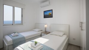 A hotel room with two beds, a window with a view of the sea, an air conditioning unit, and a framed picture on the wall. - Fall in Love With This Luxury Beachfront 1386 (Larnaca)