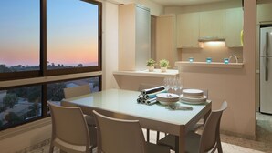 A dining area with a table set for four, a view of the sunset through large windows, and a kitchen with modern appliances. - You Will Love This Luxury Apartment With Stunning Sea Views, Larnaca Apartment 1384 (Larnaca)