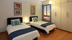 A hotel room with two beds, a nightstand, framed artwork on the wall, and a view of the sunset through a window. - You Will Love This Luxury Apartment With Stunning Sea Views, Larnaca Apartment 1384 (Larnaca)
