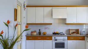 A kitchen with white cabinets, a stove, and a sink. There are decorative plants and a fruit bowl on the counter. - Seaside Serenity: Protaras Villa 1515 (Paralimni)