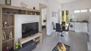 A modern living room with a flat-screen TV, wooden shelving, and a dining area with chairs and a table. - Luxury Holiday Apartment, Protaras Apartment 1417 (Paralimni)