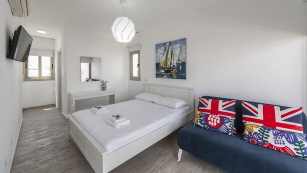 A bedroom with a bed, a bedside table, a mirror, a window, a ceiling light, and a wall with a painting. - You and Your Family Will Love This 5 Star Villa With Private Pool, Protaras Villa 1500 (Paralimni)