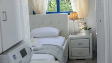 Un dormitorio con cama, una mesita de noche con lámpara y planta, y una ventana con cortinas.