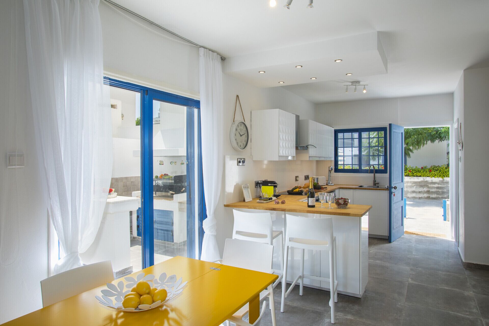 Una cocina moderna con armarios blancos, encimera de madera y un comedor con mesa amarilla y sillas blancas.