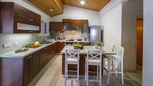 A modern kitchen with wooden cabinets, a central island with chairs, and a dining table. - You and Your Family Will Love This 5 Star Villa With Forest Views, Limassol Villa 1001 (Platres)