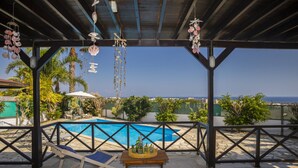 A covered outdoor pool area with a view of the sea, lounge chairs, and a table with bottles.