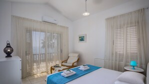Quarto de hotel com cama, uma cadeira, uma mesinha e uma luminária.
