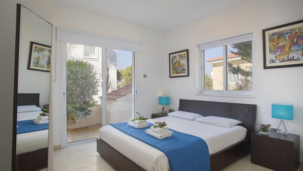 A hotel room with a bed, two bedside tables, a window, and a door leading to a balcony. - Your Beautiful Holiday Villa Minutes From Beautiful Beaches, Ayia Napa Villa 1370 (Sotira)