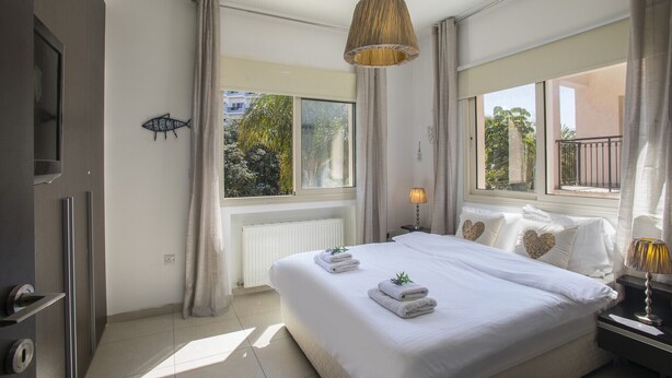 Habitación de hotel con una cama grande, dos mesitas de noche, un televisor y una ventana con vistas a zonas verdes.