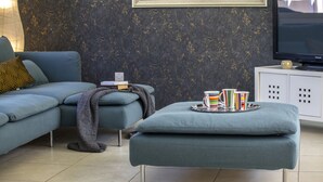 Una sala de estar con sofá, reposapiés y televisión sobre un mueble.