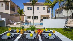 Mesa de comedor al aire libre, con piscina y un edificio de dos pisos al fondo.
