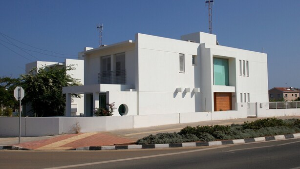 Um edifício moderno branco com telhado plano, porta de madeira e uma pequena varanda.