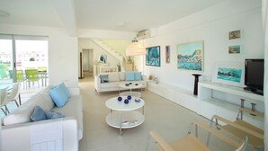 Uma sala de estar moderna com sofá, mesa de centro e cadeiras. Há uma escada que leva a outro andar, e obras de arte nas paredes.