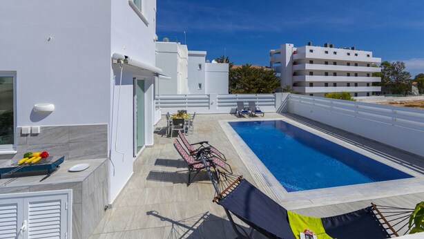 A modern building with a swimming pool, outdoor seating, and a grill area. - At Last You can Rent the Perfect Luxury Villa, Protaras Villa 1494 (Paralimni)