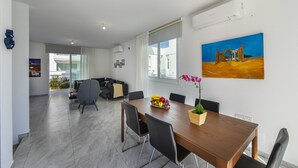A modern living room with a sofa, a dining table with chairs, and a painting on the wall. - At Last You can Rent the Perfect Luxury Villa, Protaras Villa 1494 (Paralimni)
