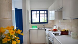 Una cocina compacta con armarios blancos, un ventanal con marco azul, un lavabo y un tostador.