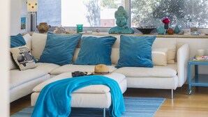 Een moderne woonkamer met een witte bank, blauwe kussens, een blauwe plaid en een klein tafeltje met decoratieve items.