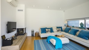 Een moderne woonkamer met een witte bank, blauwe kussens, een flatscreen televisie en een open haard.