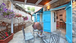 A patio with two metal chairs, a table, and hanging flower baskets. - Charming Stone Cottage Getaway - Nicosia 1003 (Kalopanayiotis)
