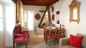 A cozy living room with a wooden ceiling, a dining table set for four, and a red sofa. - Charming Stone Cottage Getaway - Nicosia 1003 (Kalopanayiotis)