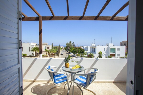 A balcony with a table, chairs, and a view of the sea and buildings. - Indulge in Luxury Living Steps From the Beach,1419 (Paralimni)