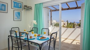 A dining area with a table set for four, featuring croissants and orange juice, overlooking a residential area with a clear view of the sea. - Indulge in Luxury Living Steps From the Beach,1419 (Paralimni)