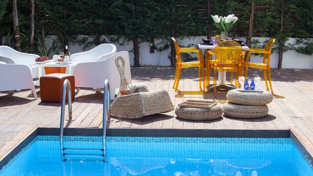 Un espace piscine équipé d’un échelle, de chaises longues blanches, de chaises jaunes et de poufs en osier.